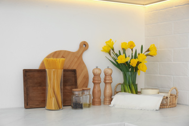 Photo of Wooden kitchenware, spaghetti and narcissus flowers on counter indoors