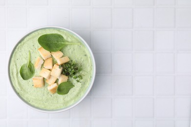 Delicious spinach cream soup with croutons in bowl on white tiled table, top view. Space for text