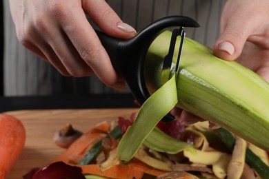 Photo of Woman peeling fresh zucchini at table, closeup