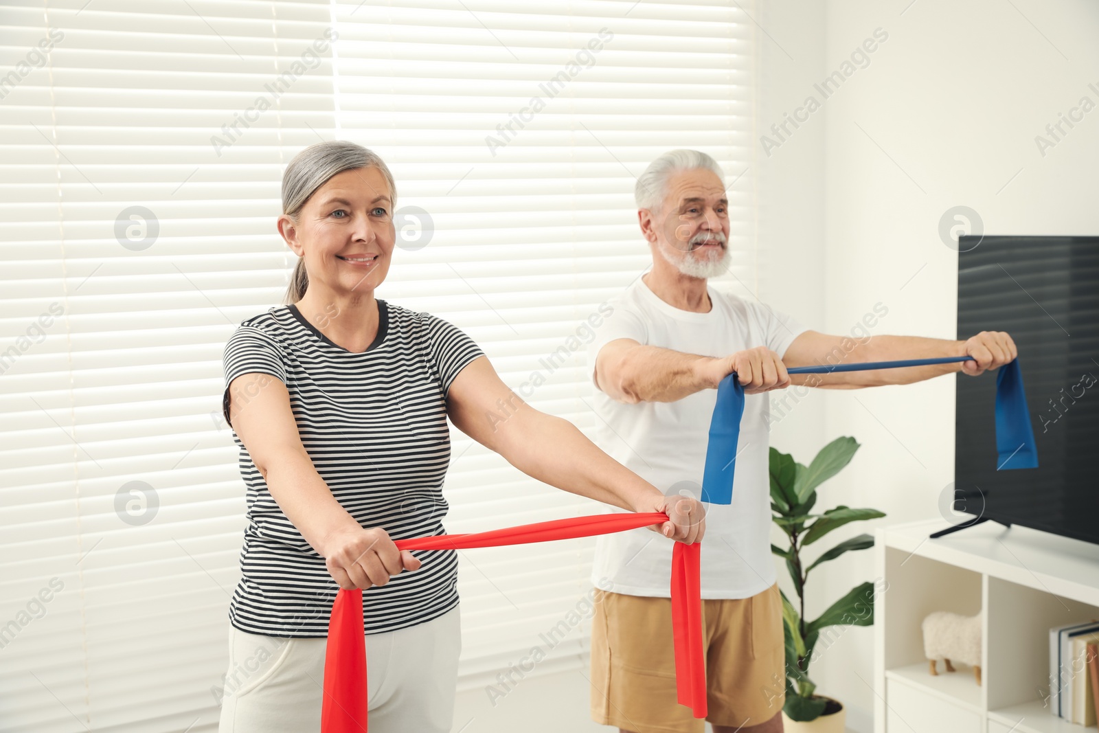 Photo of Senior couple doing exercise with fitness elastic bands at home, selective focus