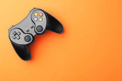 Wireless game controller on orange background, top view. Space for text
