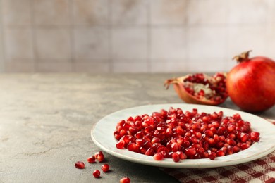 Photo of Tasty ripe pomegranate grains on grey table. Space for text