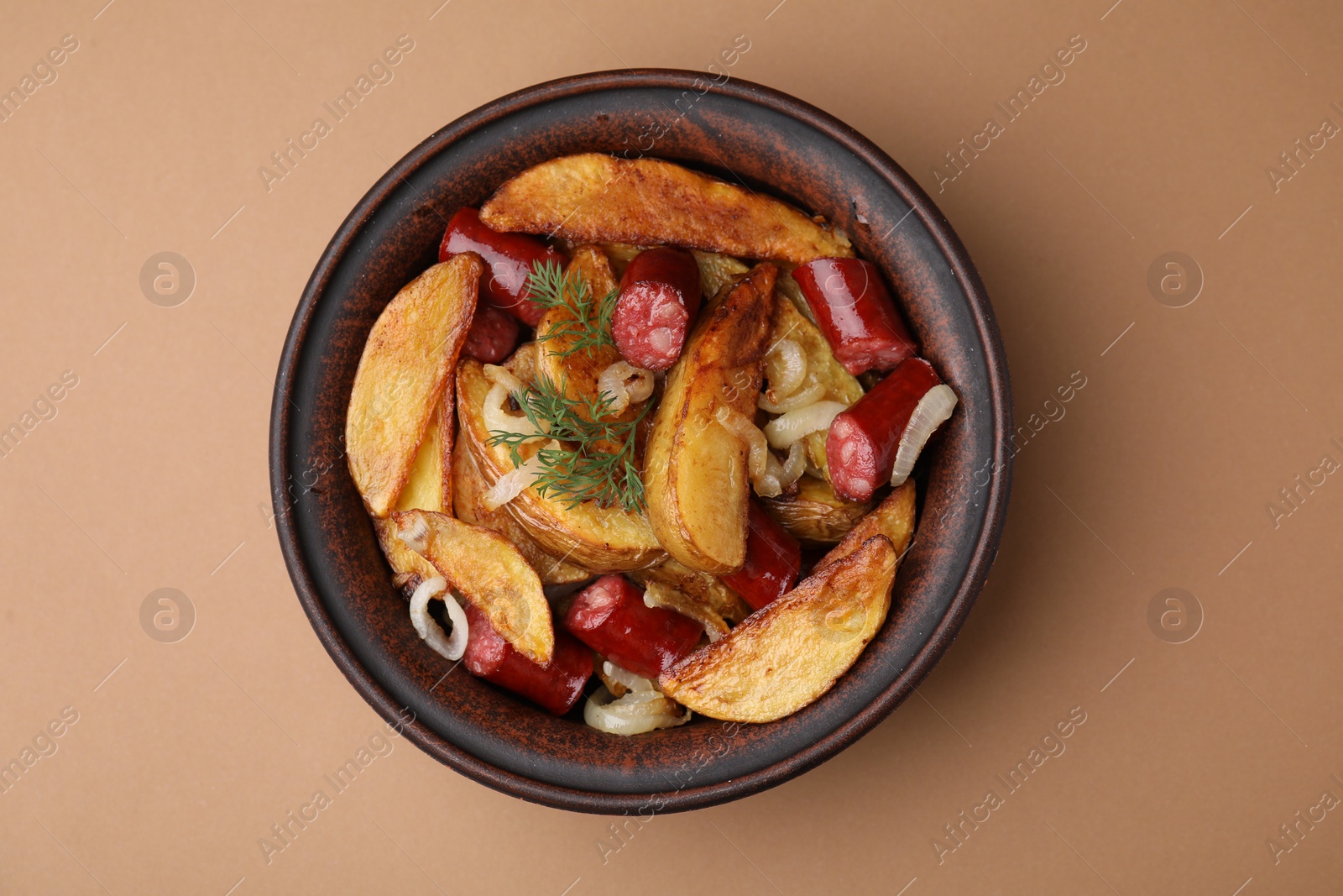 Photo of Delicious baked potato with thin dry smoked sausages, onion and dill in bowl on light brown table, top view