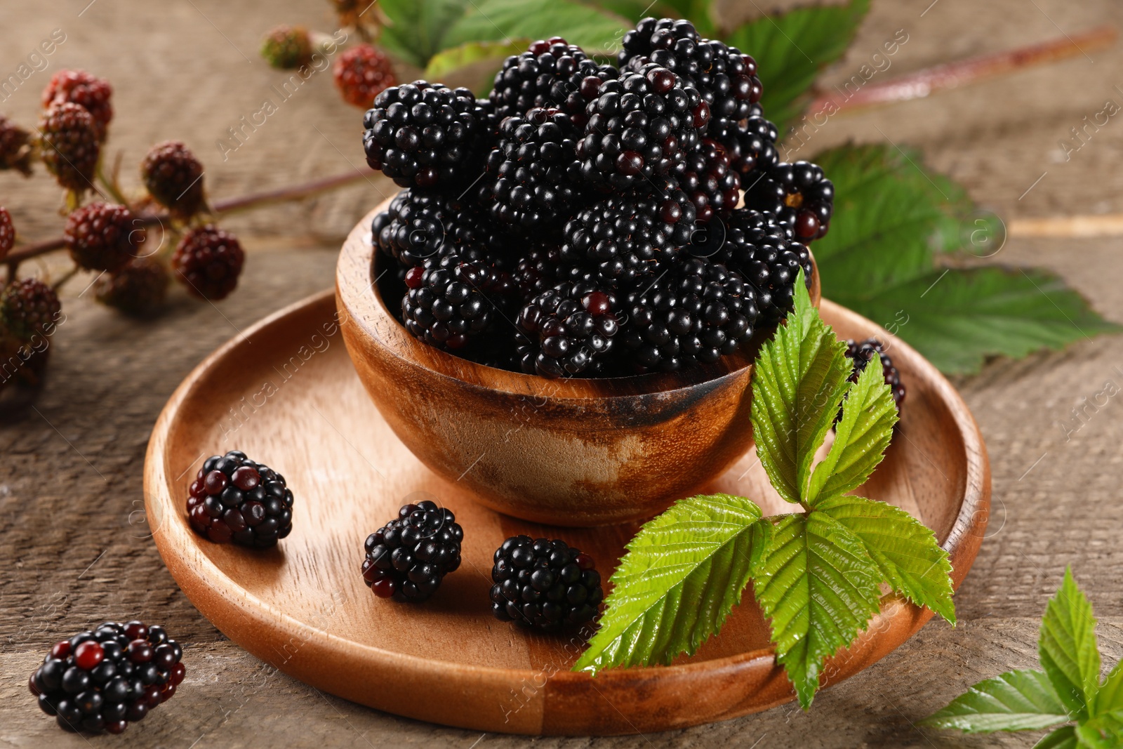 Photo of Fresh ripe blackberries and leaves on wooden table, closeup