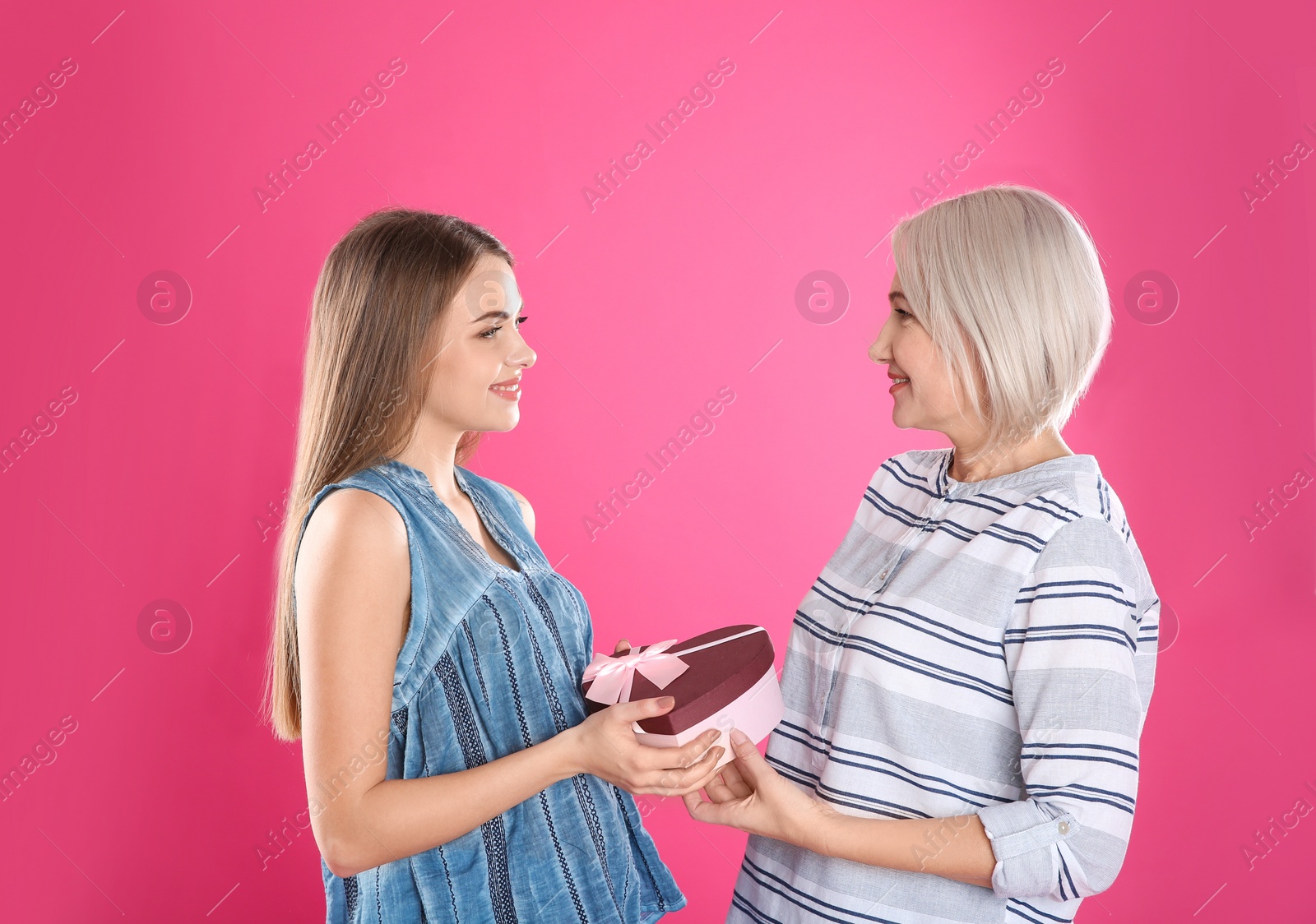 Photo of Young daughter congratulating her mature mother on color background. Happy Women's Day