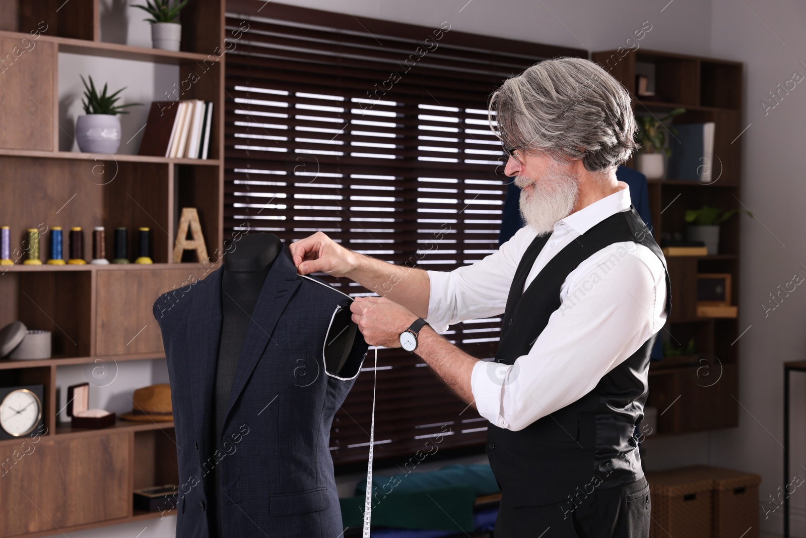 Photo of Professional tailor with measuring tape working in atelier