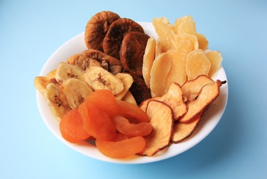 Photo of Bowl with different dried fruits on light blue background