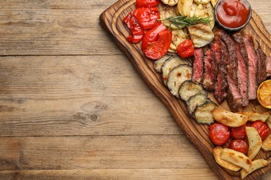 Delicious grilled beef with vegetables, spices and tomato sauce on wooden table, top view. Space for text