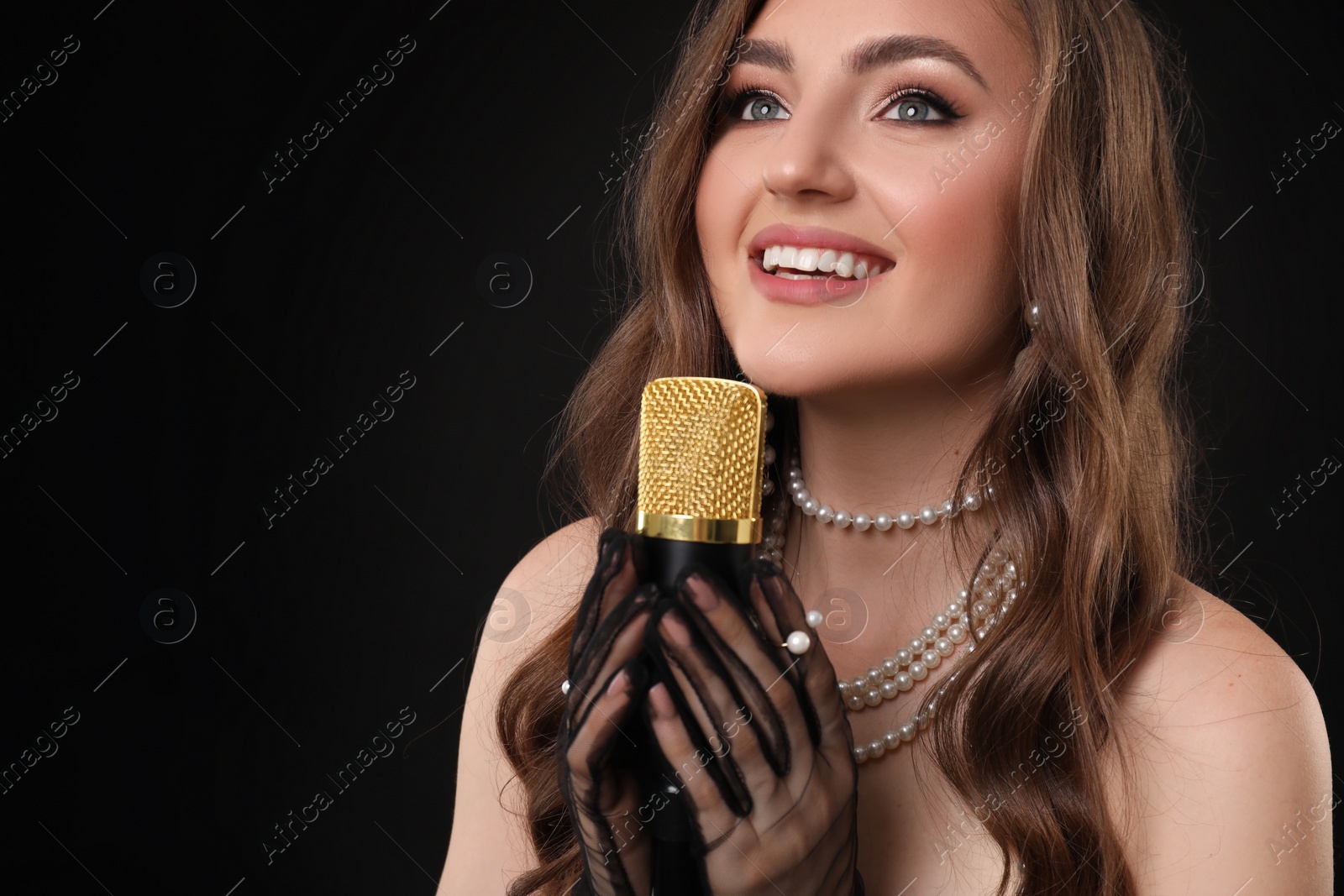 Photo of Beautiful young jazz singer with microphone on black background