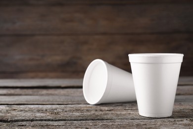 Two white styrofoam cups on wooden table, space for text
