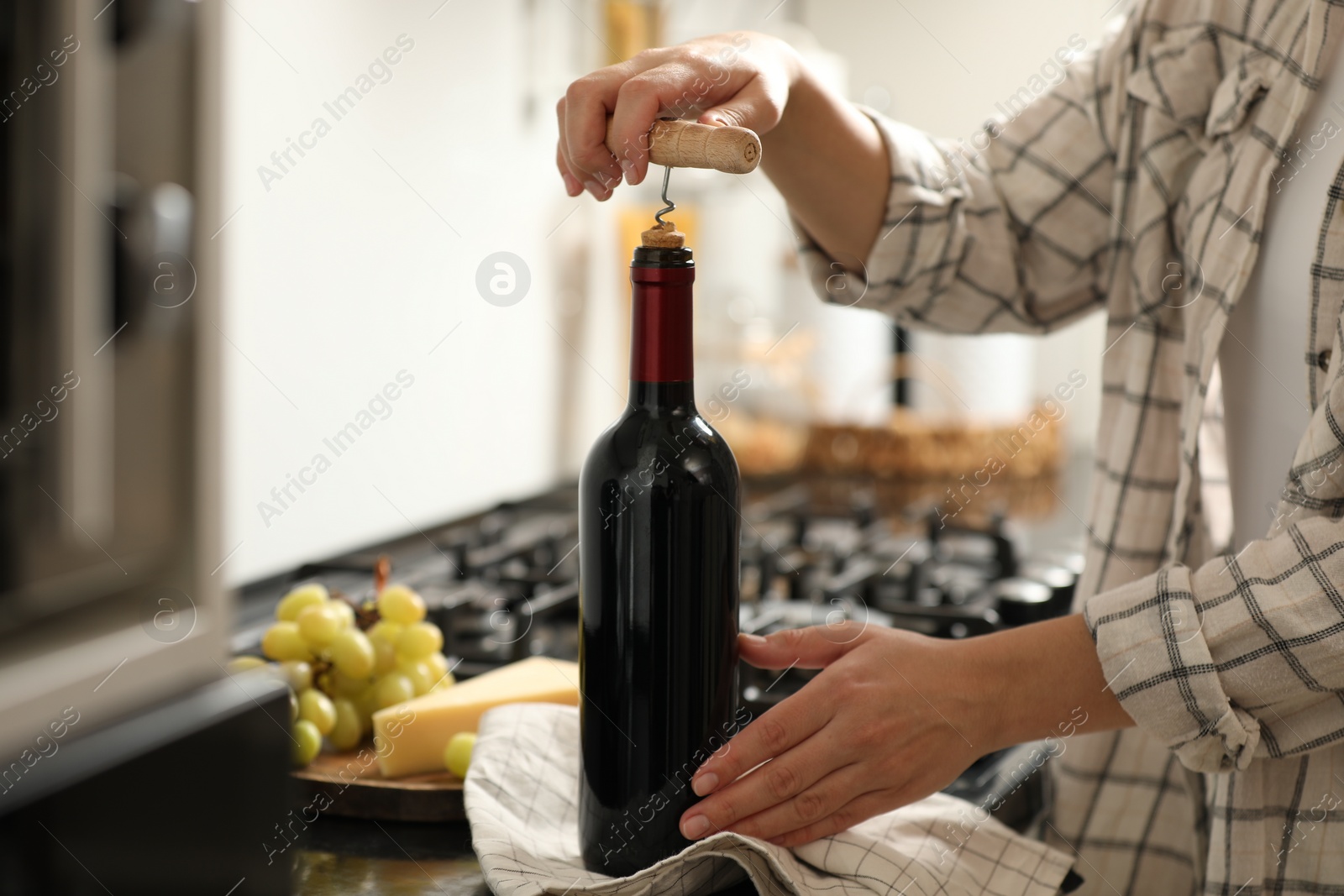 Photo of Woman opening wine bottle with corkscrew at countertop indoors, closeup