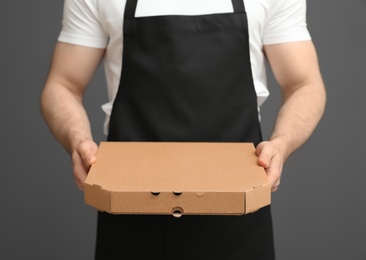 Photo of Waiter in apron with pizza box on grey background, closeup. Food delivery service