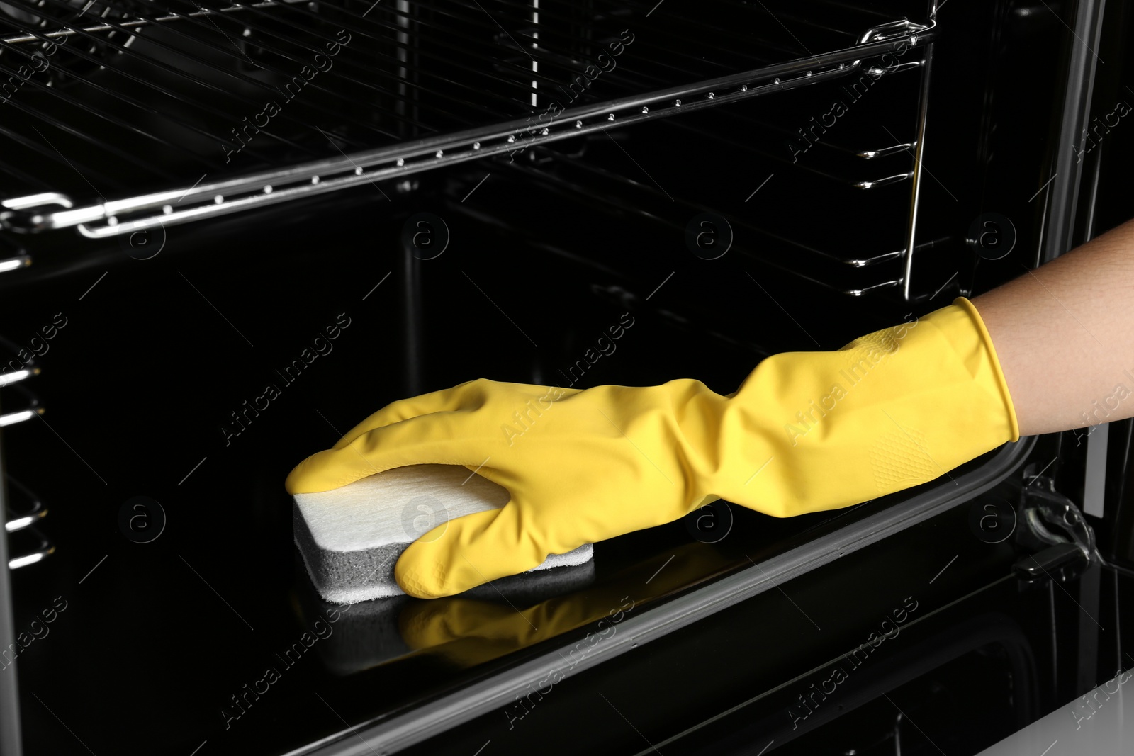 Photo of Woman cleaning electric oven with sponge, closeup