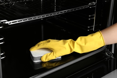 Photo of Woman cleaning electric oven with sponge, closeup