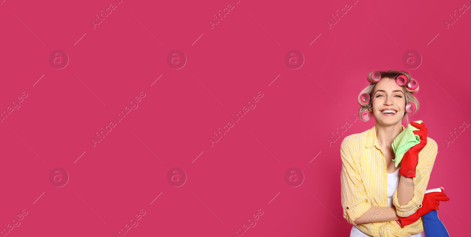 Photo of Young housewife with detergent and rag on pink background. Space for text