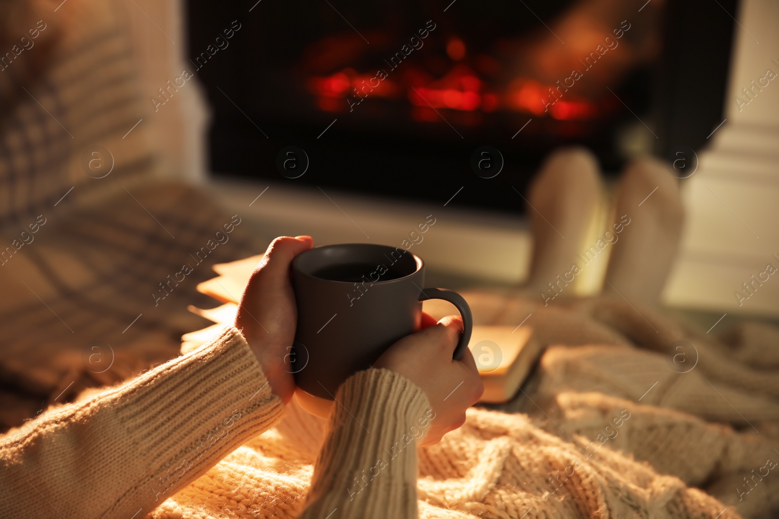 Photo of Woman with cup near fireplace indoors, closeup. Cozy atmosphere