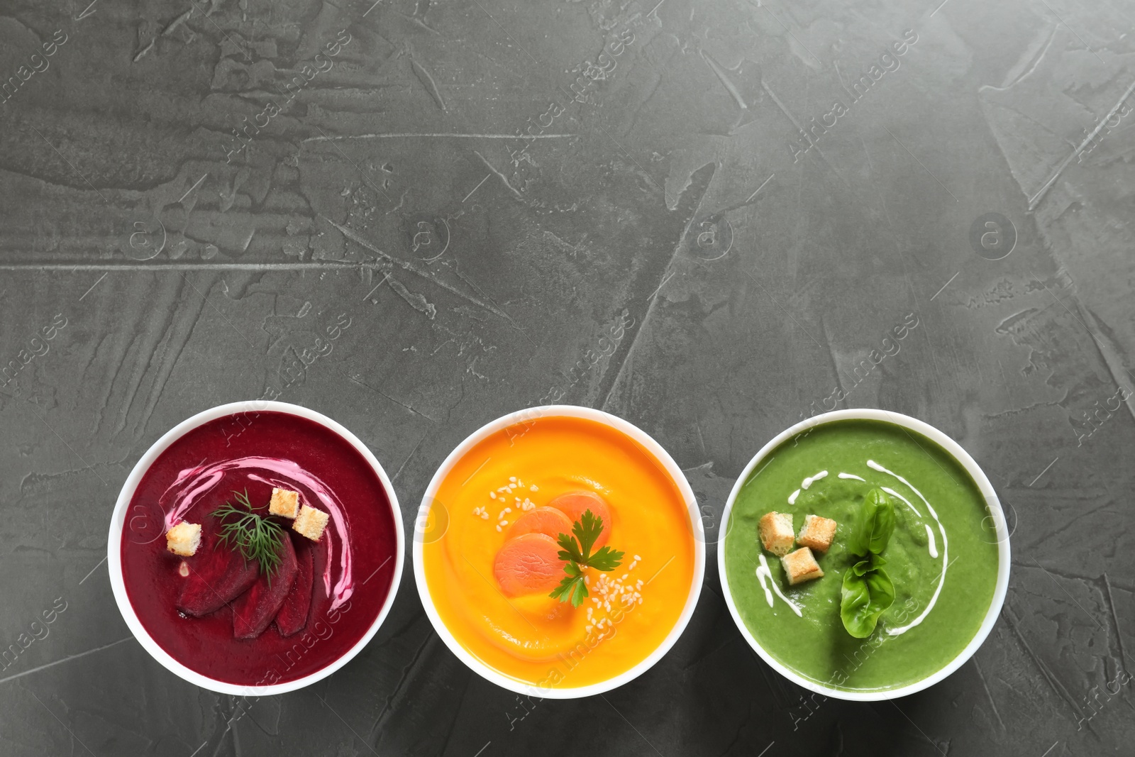 Photo of Various cream soups in bowls and space for text on grey background, top view