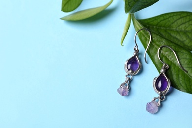 Photo of Beautiful pair of silver earrings with amethyst gemstones and leaves on light blue background, above view. Space for text