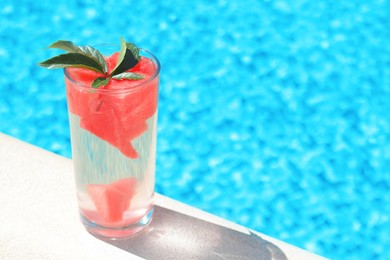 Photo of Refreshing watermelon drink in glass near swimming pool outdoors. Space for text