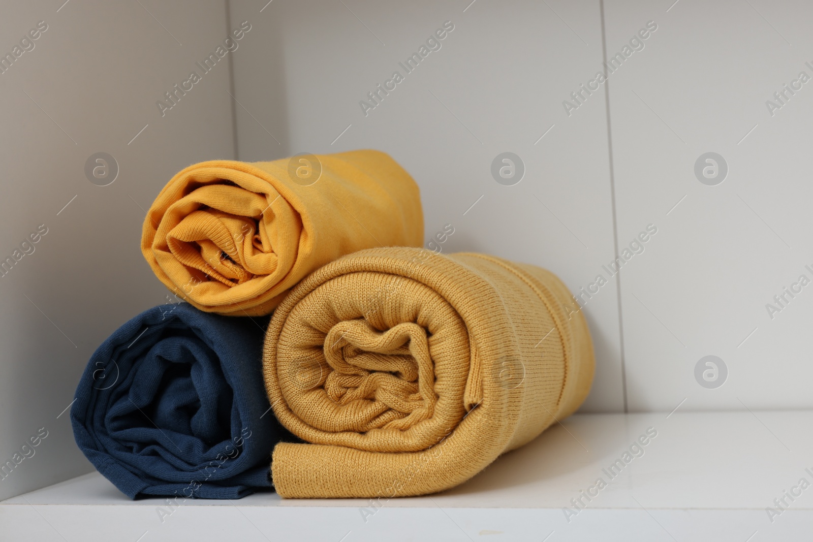 Photo of Different rolled shirts on white shelf. Organizing clothes