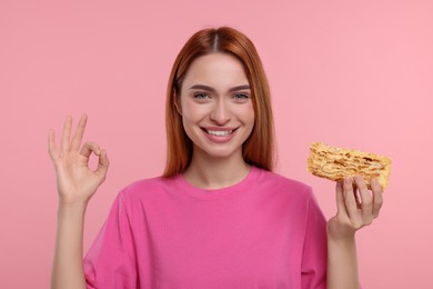 Photo of Young woman with piece of tasty cake showing ok gesture on pink background