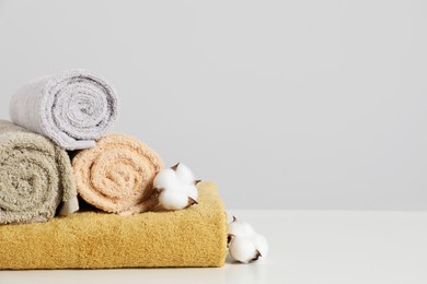Photo of Clean soft towels with cotton flowers on white table against light grey background. Space for text