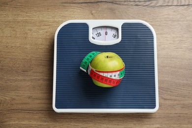 Photo of Scales with apple and measuring tape on wooden table, top view. Weight loss