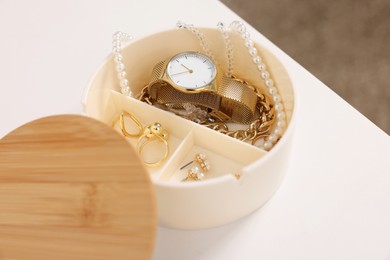 Jewelry box with wristwatch and accessories on white table, closeup