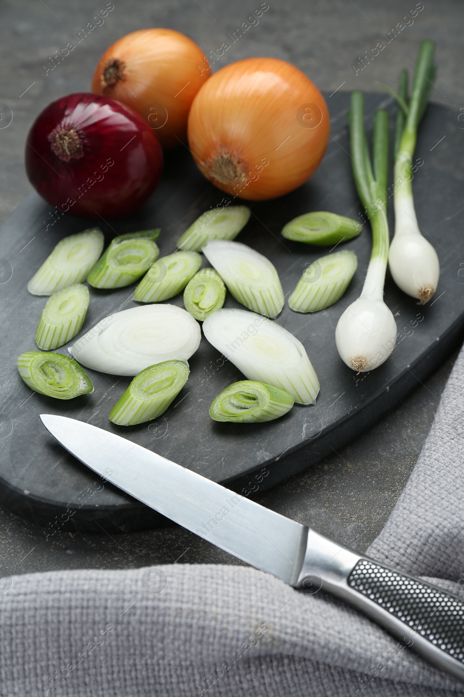 Photo of Board with different kinds and knife of onions on grey table, closeup