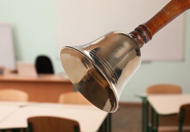 Image of Golden school bell with wooden handle and blurred view of empty classroom