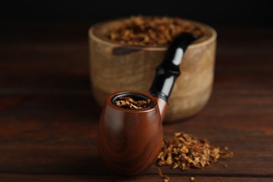 Smoking pipe and dry tobacco on wooden table, closeup