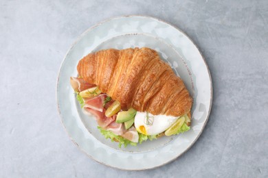 Photo of Delicious croissant with prosciutto, avocado and egg on grey table, top view