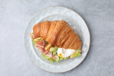 Delicious croissant with prosciutto, avocado and egg on grey table, top view