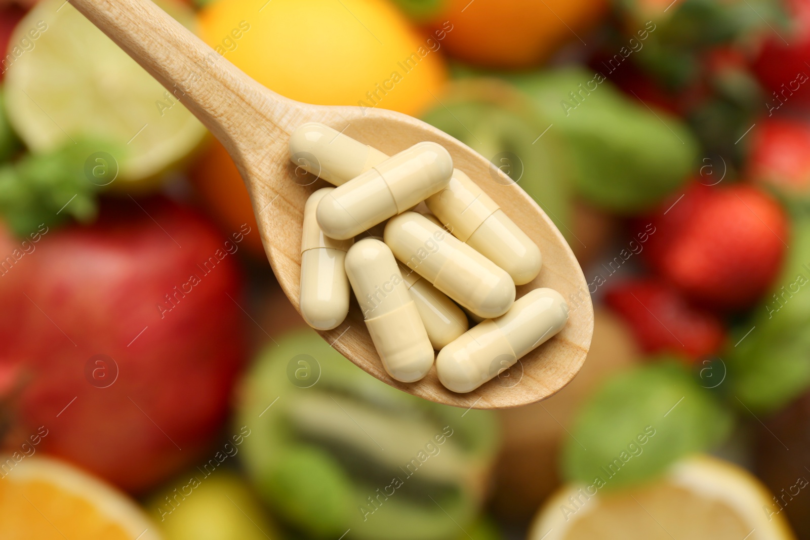 Photo of Vitamin pills in spoon over fresh fruits, top view