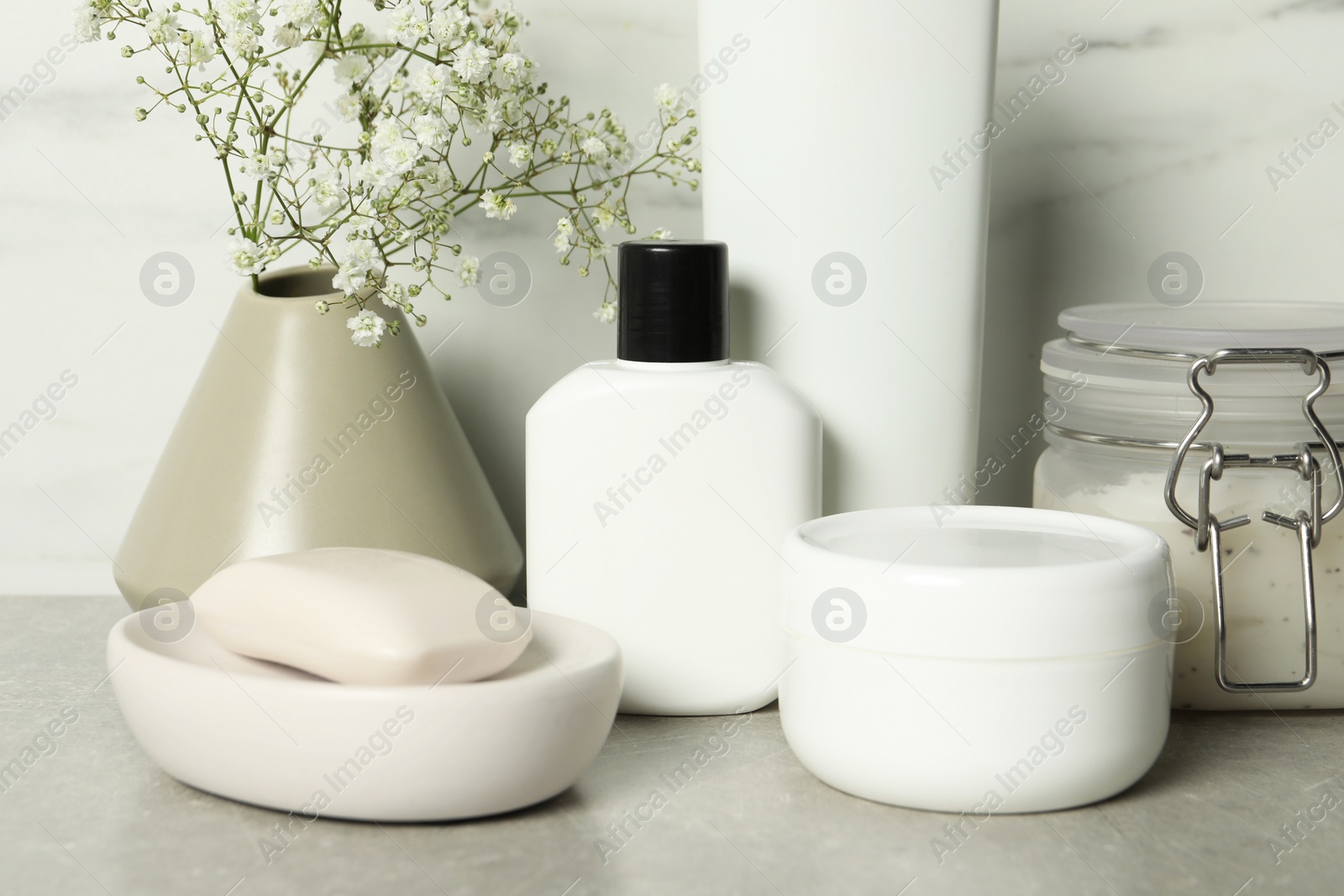 Photo of Bath accessories. Personal care products and gypsophila flowers in vase on gray table, closeup