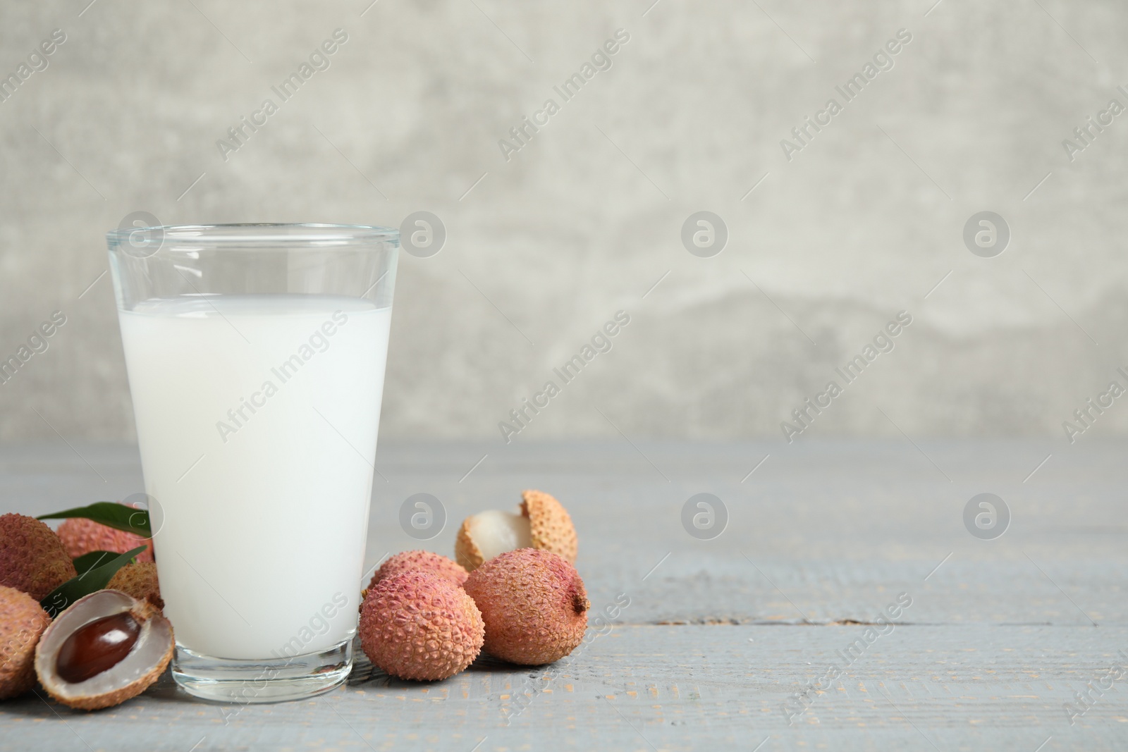 Photo of Fresh lychee juice and fruits on grey wooden table. Space for text