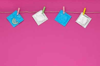 Clothesline with packaged condoms on pink background, space for text. Safe sex