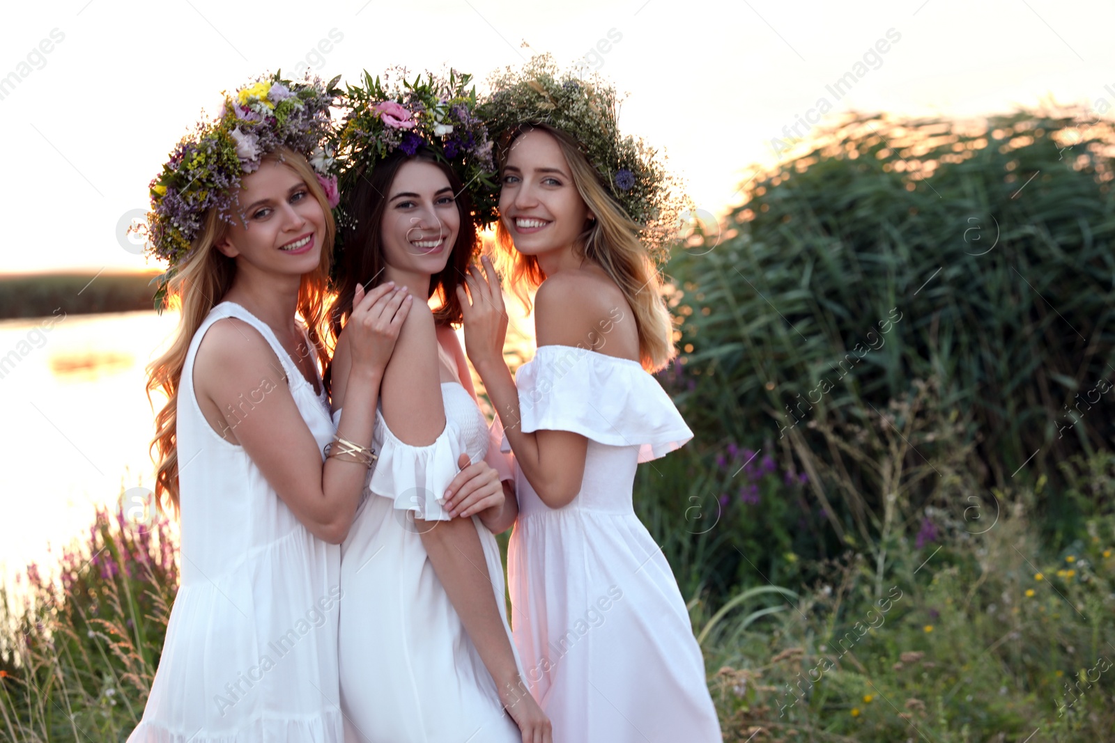 Photo of Young women wearing wreaths made of beautiful flowers outdoors at sunset