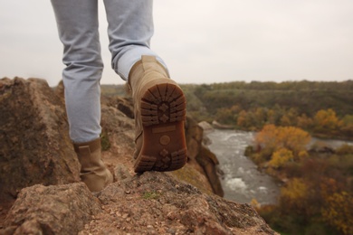 Photo of Woman wearing stylish hiking boots on steep cliff, closeup