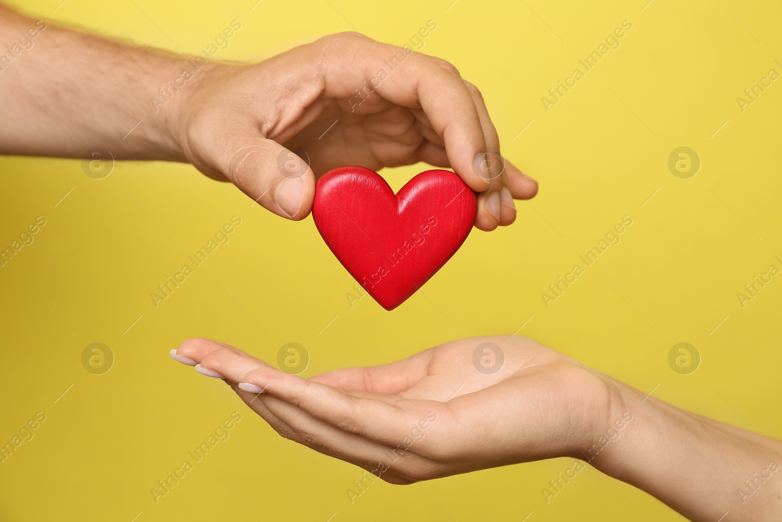 Photo of Man giving red heart to woman on yellow background, closeup. Donation concept