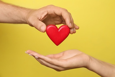 Man giving red heart to woman on yellow background, closeup. Donation concept