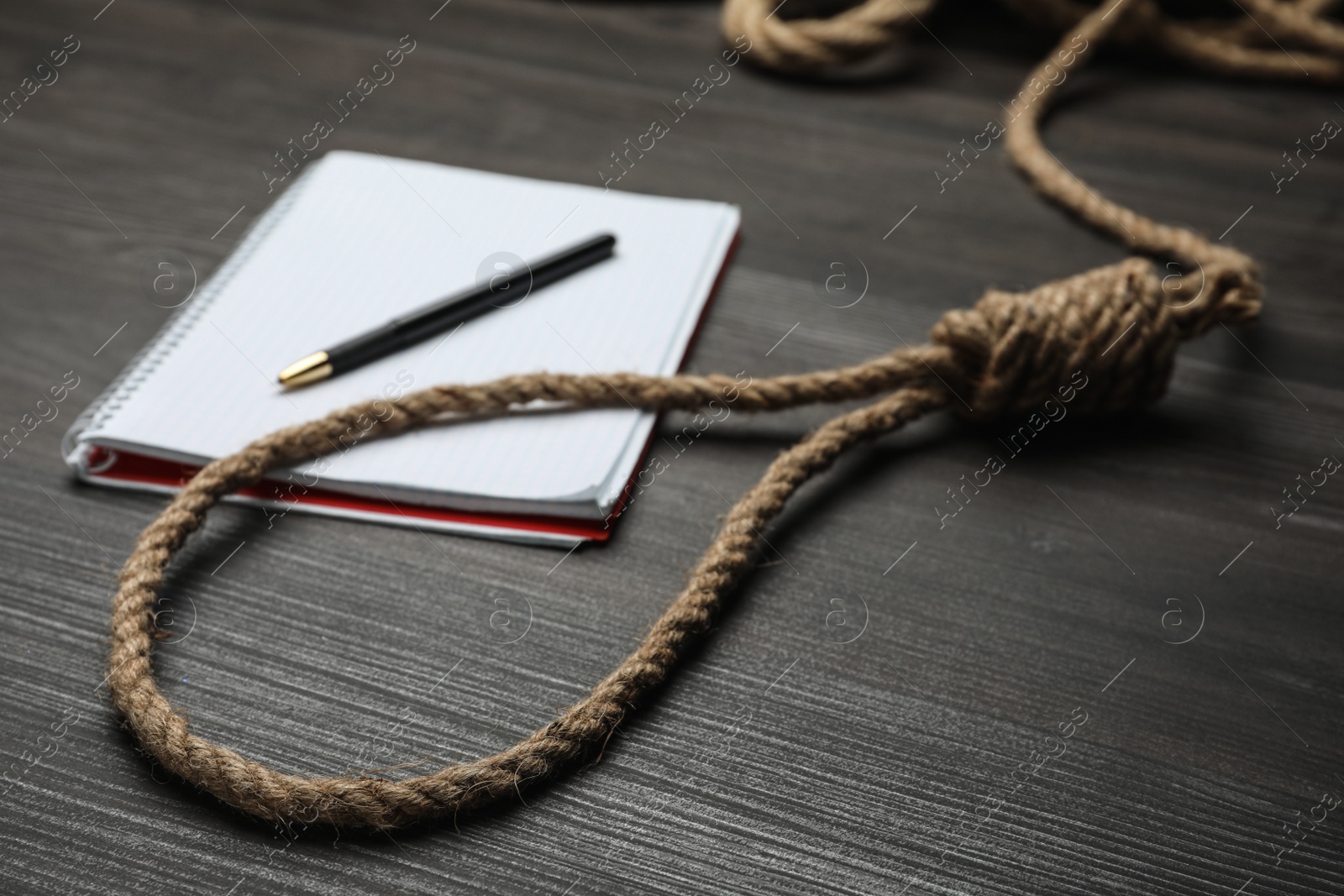 Photo of Rope noose and blank notebook with pen on black wooden table, closeup