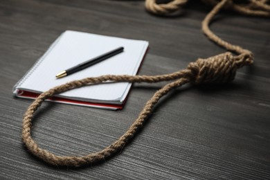 Rope noose and blank notebook with pen on black wooden table, closeup