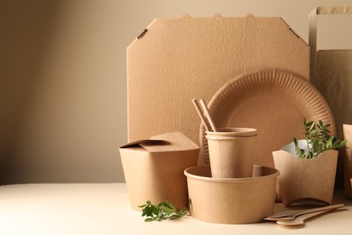 Eco friendly food packaging. Paper containers, tableware, bag and green twigs on white table against beige background. Space for text