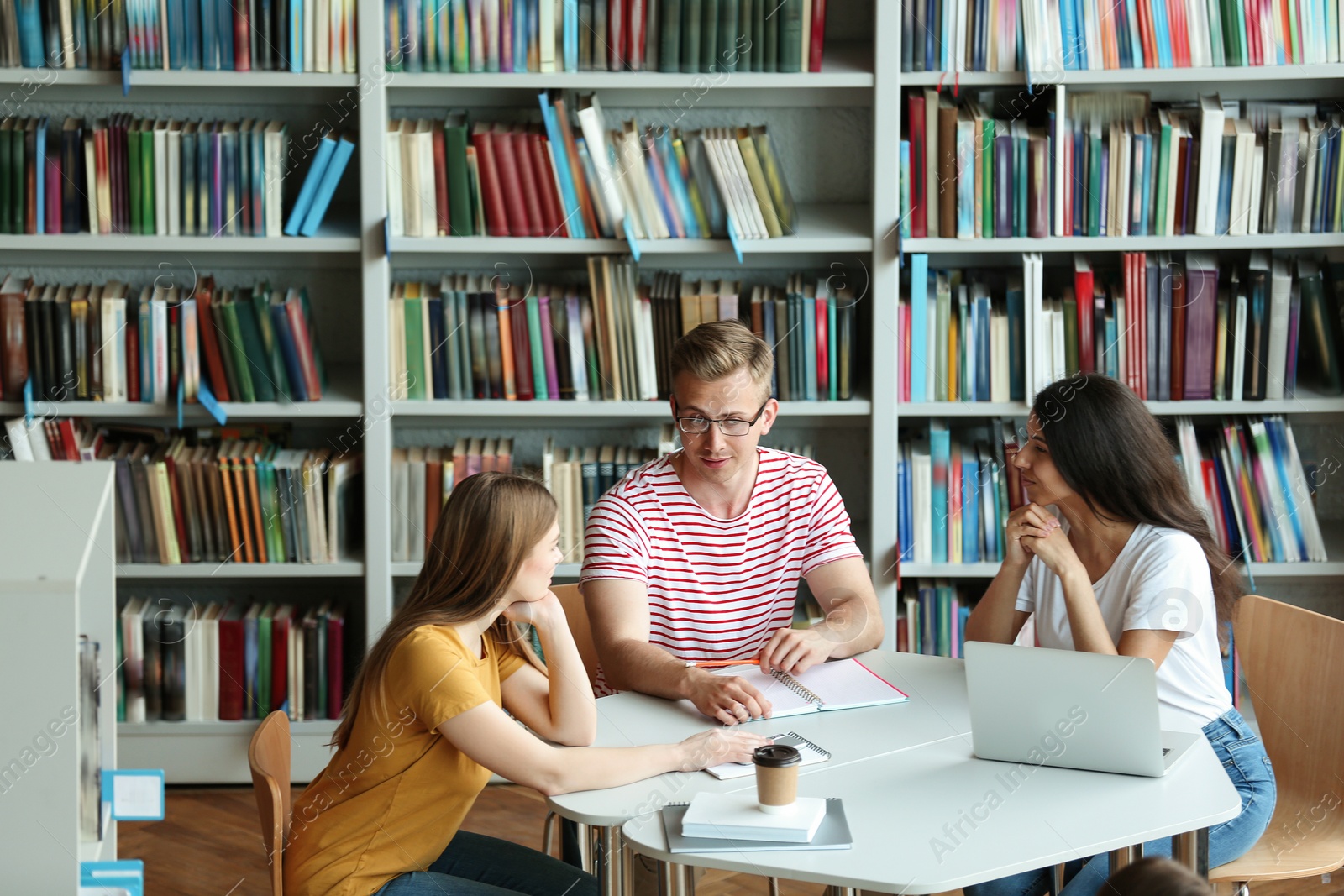 Photo of Young people discussing group project at table in library