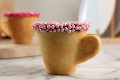 Photo of Delicious edible biscuit cup decorated with sprinkles on white marble table, closeup