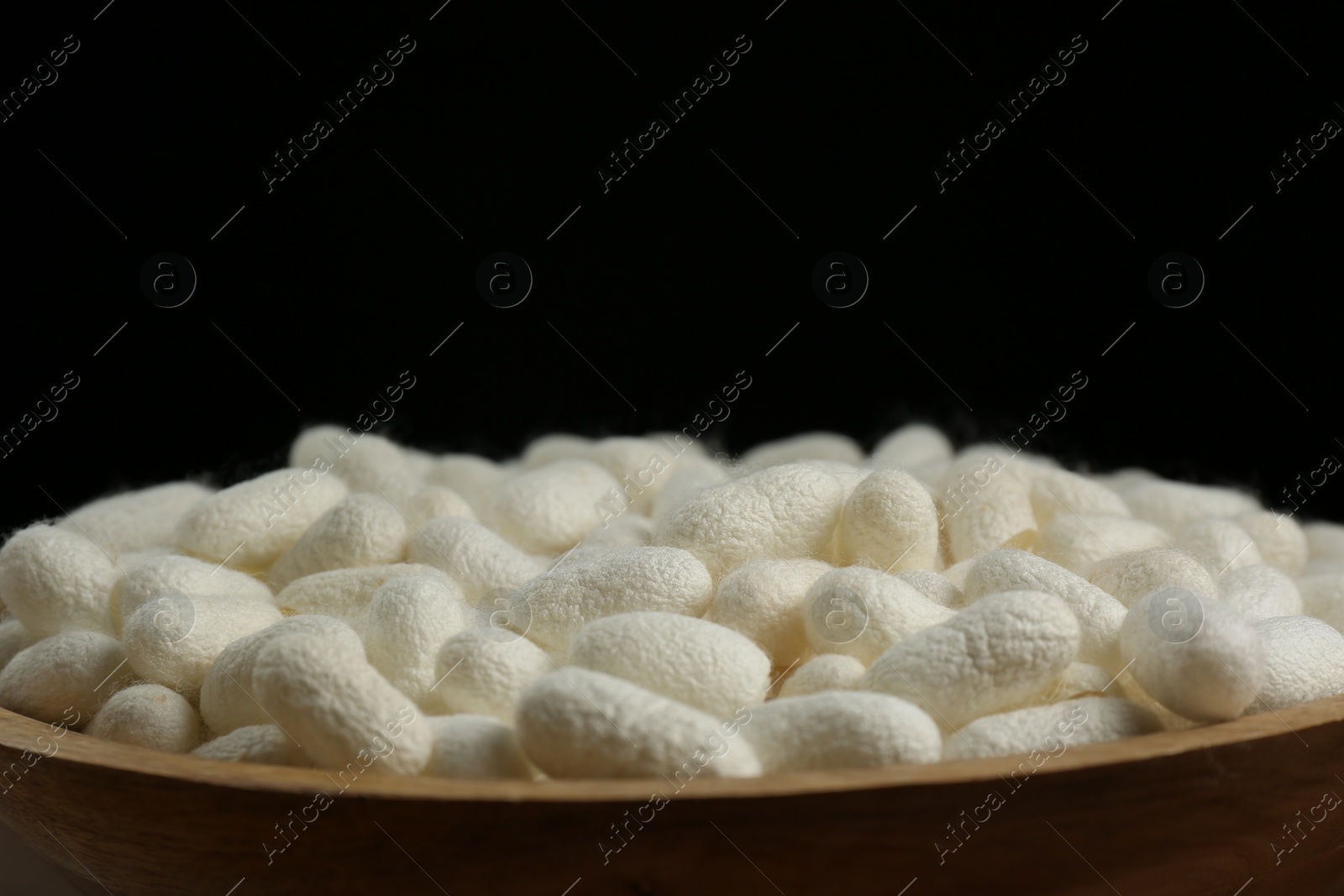 Photo of White silk cocoons in wooden bowl on black background, closeup