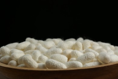 White silk cocoons in wooden bowl on black background, closeup