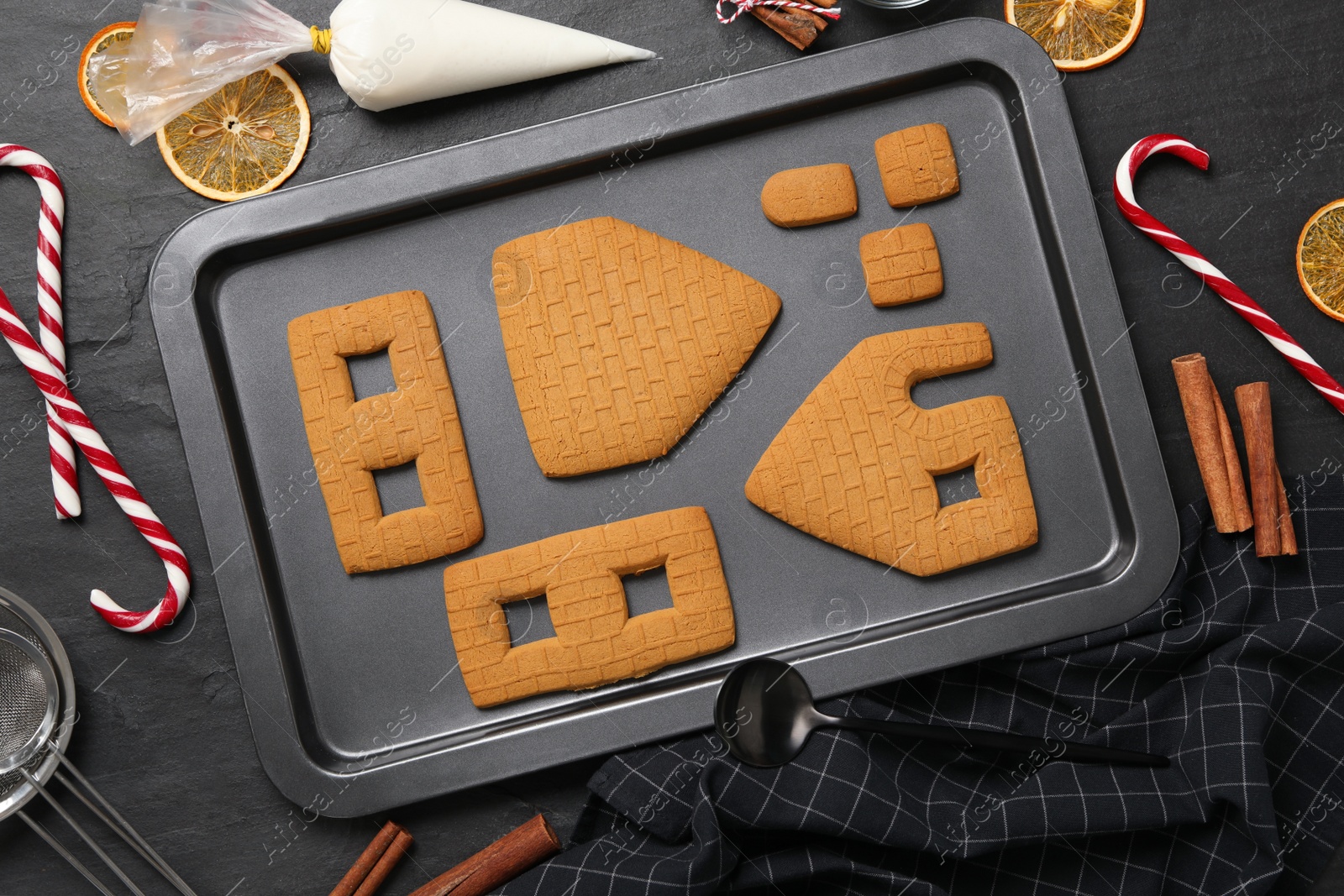 Photo of Parts of gingerbread house, kitchenware and ingredients on black table, flat lay