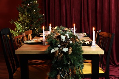 Dining table with burning candles and Christmas decor in stylish room. Interior design